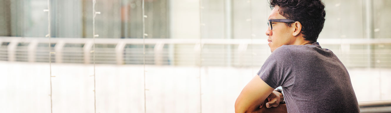 A young man is leaning on a balcony railing and looking out into the distance.