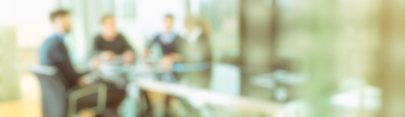 A defocused picture of 4 people sitting at a conference table.