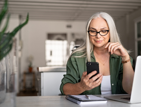 A woman using computer and phone at kitchen counter