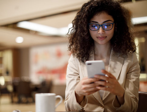 A woman with coffee looks at her cellphone.