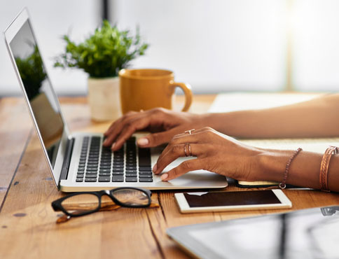 An unrecognizable woman is sitting at a table using a laptop.