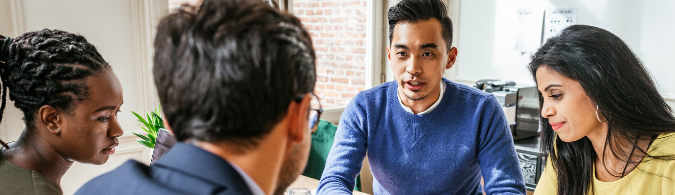 A group of four young business people are sitting at a table having a discussion.