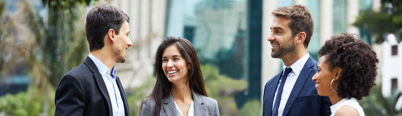 Four young business people are standing outside talking and smiling.