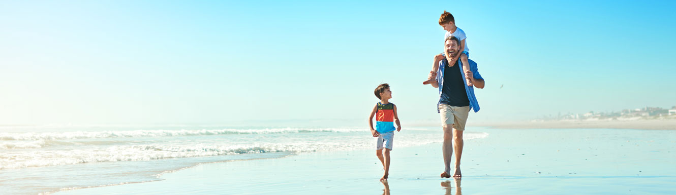 A father and his two young sons are seen walking on the beach.