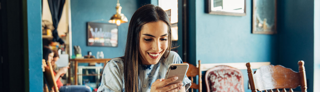 A young woman is sitting in a brightly colored cafe and using her cellphone.