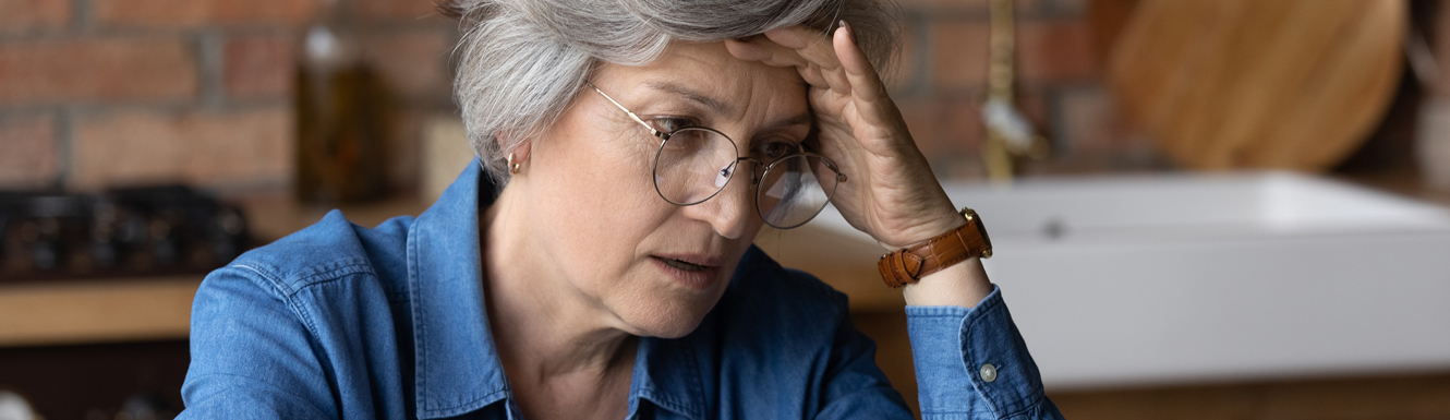 A mature woman in glasses who is in distress and has her hand on her forehead.