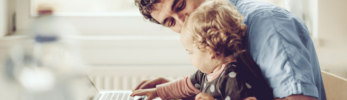 A father and his infant daughter are looking at a laptop against a bright background.