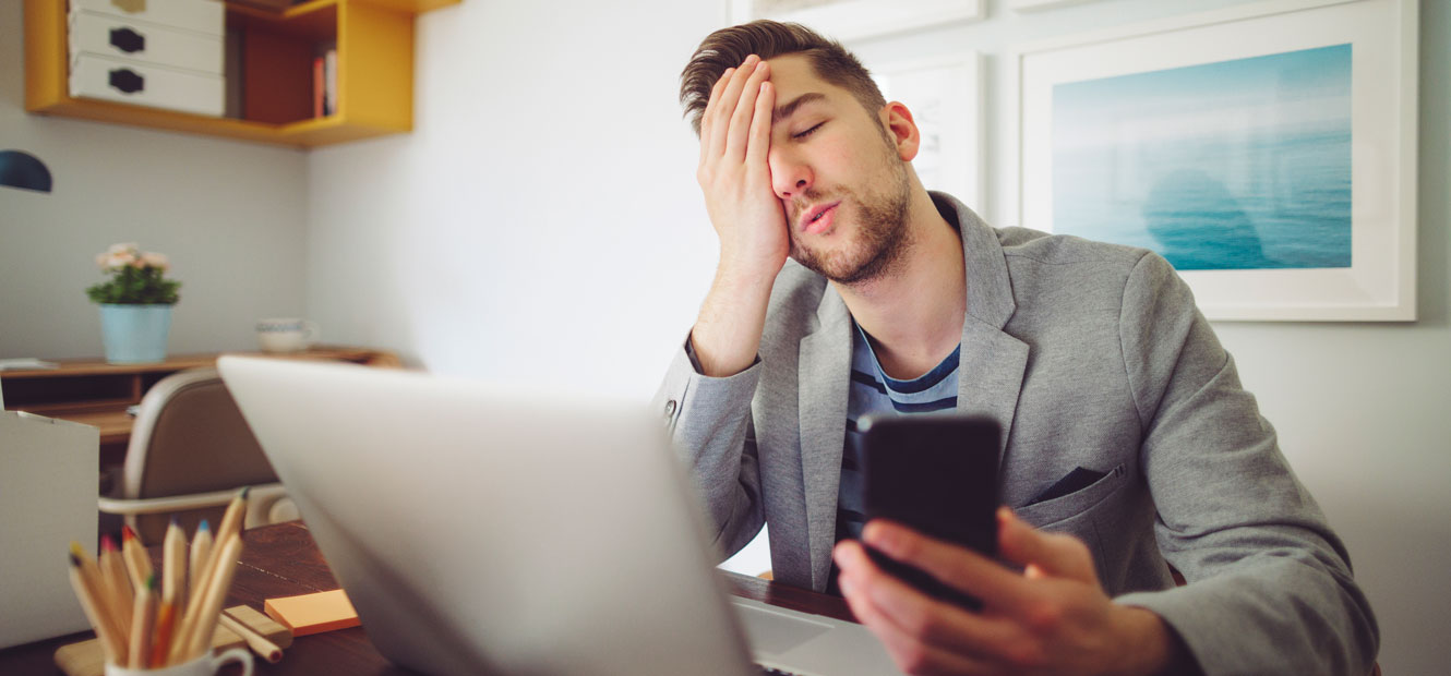 A young man looks distraught from what he saw on his computer and cell phone.