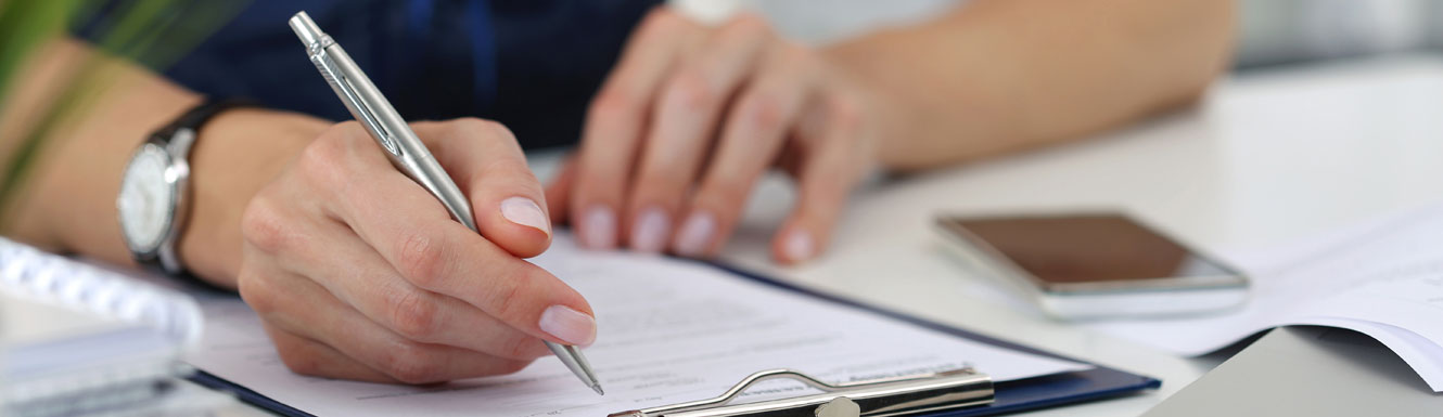 A woman's hand can be seen filling out paperwork on a clipboard.