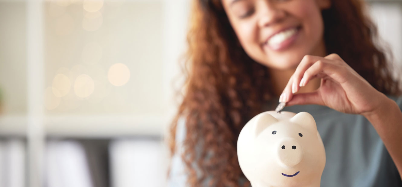 A young woman is smiling and placing a coin in a piggy bank.